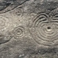 Petroglifos de Mogor: grabados circulares concéntricos y un posible sol en una roca antigua.