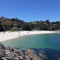 Gente disfrutando del sol y el mar en la playa San Xian, con casas en la colina verde.