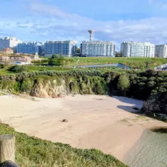 Playa en el parque de bens, con arena dorada, acantilados verdes y edificios modernos al fondo.