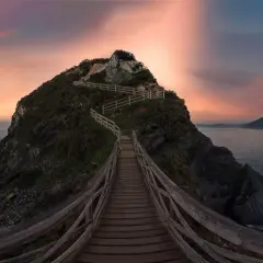 Pasarela de madera serpentea hacia la cima de un acantilado en Galicia, con el mar y un cielo crepuscular de ensueño. Unos de los miradores más espectaculares.