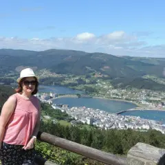 Mujer con sombrero blanco y blusa rosa posa en el mirador de San Roque, disfrutando de la vista panorámica de la ría y el pueblo.