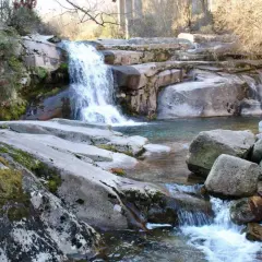 Cascada y charcas naturales en Ourense, rodeadas de rocas cubiertas de musgo y vegetación.