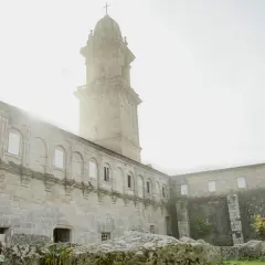 El imponente **monasterio de Oia** se alza bajo un cielo brumoso, con su torre campanario y sus muros de piedra evocando historias de siglos pasados.