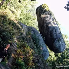 Hombre sonriente junto a una roca suspendida, un ejemplo de la pena do equilibrio en la naturaleza.