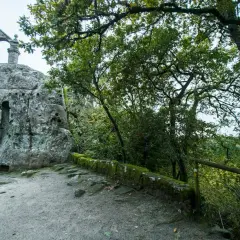 Antigua ermita rupestre de San Pedro de Rocas, con su estructura de piedra y arcos, rodeada de vegetación frondosa.