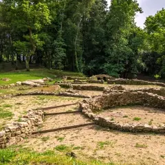 Ruinas de un castro alobre, con muros de piedra y vegetación exuberante.