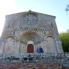 Dos personas posan frente a la fachada románica de Santo Estevo de Ribas de Miño, con su rosetón y portal detallados.