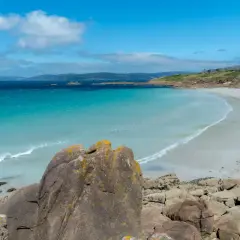 Aguas turquesas y arena blanca en una de las hermosas playas de la Costa da Morte. Rocas cubiertas de líquenes en primer plano.