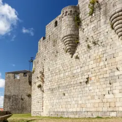 Muros de piedra de un castillo medieval en Castro Caldelas. Un torreón con matacanes y una torre con reloj son parte de lo que ver.