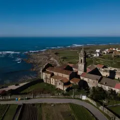Monasterio de Santa María de Oia, con su torre campanario y tejados rojizos, se alza majestuoso junto al mar Cantábrico.