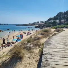 Gente disfrutando del sol y el mar en la playa Pedras Negras. Un camino de madera bordea la arena dorada y las dunas.