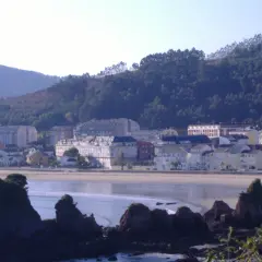 Vista de la playa vivero con edificios y colinas verdes al fondo.