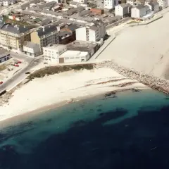 Vista aérea de la playa Penoural en Burela, con edificios urbanos y el mar azul turquesa.