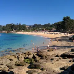 Gente disfrutando del sol y el mar en la Praia da Mourisca, con aguas cristalinas y arena dorada.