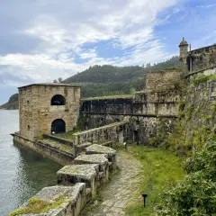 El castillo San Felipe en Ferrol, una fortaleza de piedra junto al mar, con vegetación cubriendo sus muros y un camino empedrado.
