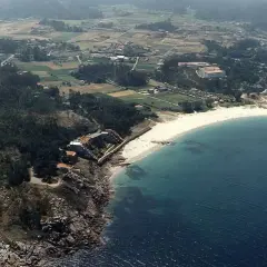 Vista aérea de la **playa de Cabeiro**, con arena blanca, aguas turquesas y un paisaje rural salpicado de casas y vegetación.