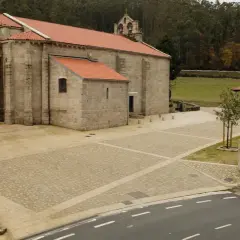 El monasterio de Soandres, con su piedra gris y tejados rojos, se alza majestuoso ante un bosque frondoso. Un cruceiro de piedra vigila la plaza empedrada.
