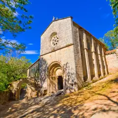 Monasterio de Santa Cristina de Ribas de Sil, una joya románica rodeada de exuberante vegetación bajo un cielo azul intenso.