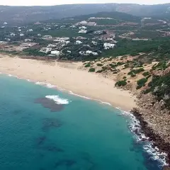 Vista aérea de la playa de los alemanes en Foz, con casas blancas dispersas entre la vegetación y el mar turquesa.