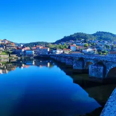 Puente de piedra en Ponte Sampaio, con casas reflejándose en el río azul bajo un cielo despejado.