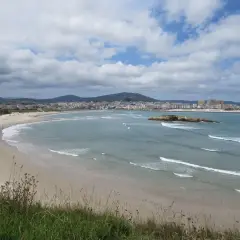 Amplia vista de la playa de Altar Barreiros con arena dorada, mar azul y una ciudad costera al fondo.