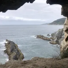Vista desde la cova da doncela. El mar agitado choca contra las rocas mientras una vela solitaria navega en el horizonte.