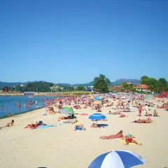 Día soleado en la playa Santa Marta de Baiona, con mucha gente disfrutando del mar y la arena bajo sombrillas.