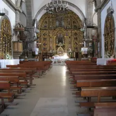 Interior de una iglesia con bancos de madera y un retablo dorado. Una pequeña maqueta de barco cuelga del techo, quizás en honor a la virxe da barca.
