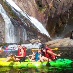 Familia disfrutando en kayak frente a la impresionante fervenza de Ézaro, con cascadas cayendo sobre rocas.