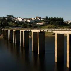 El puente de Portomarín cruza un embalse, con un pueblo en la colina al fondo.