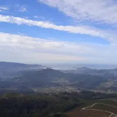 Vista panorámica desde el monte Galiñeiro, con un valle salpicado de casas y el mar al fondo bajo un cielo nublado.