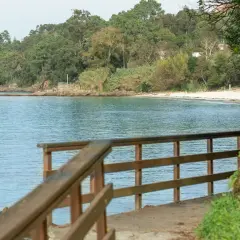 Camino de madera hacia la playa Mogor, con el mar azul y la costa verde al fondo.