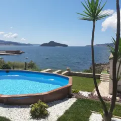 Piscina azul con vistas al mar y a la playa de Limens. Palmeras y césped verde rodean la zona de descanso.