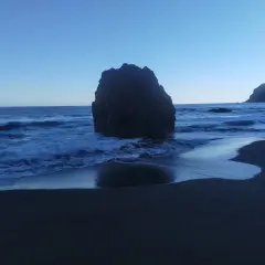 Olas rompen contra una gran roca en la playa los patos. El cielo azul claro se funde con el mar.