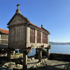 Hórreos de Combarro, construcciones de piedra con tejados rojos y cruces, se alzan sobre pilares junto al mar azul.