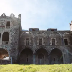 El imponente castillo de Arnado, con sus arcos y torres de piedra, se alza sobre un prado verde bajo un cielo azul.