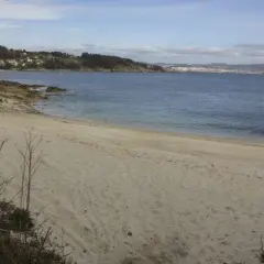 Arena dorada en la playa temperans, con el mar azul y una ciudad al fondo.