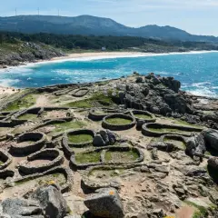 Ruinas circulares de un castro gallego junto a una playa de aguas turquesas. Paisajes de Galicia que evocan historia y naturaleza.