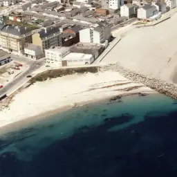 Vista aérea de la playa Penoural en Burela, con edificios urbanos y el mar azul turquesa.