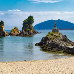 Rocas emergiendo del mar azul, un monumento en una de ellas, y la arena dorada de las playas cerca de Viveiro.