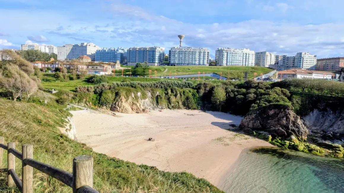 Playa en el parque de bens, con arena dorada, acantilados verdes y edificios modernos al fondo.