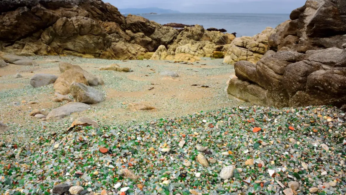La praia dos cristais, una playa de guijarros de vidrio pulido por el mar, rodeada de rocas y con el océano al fondo.