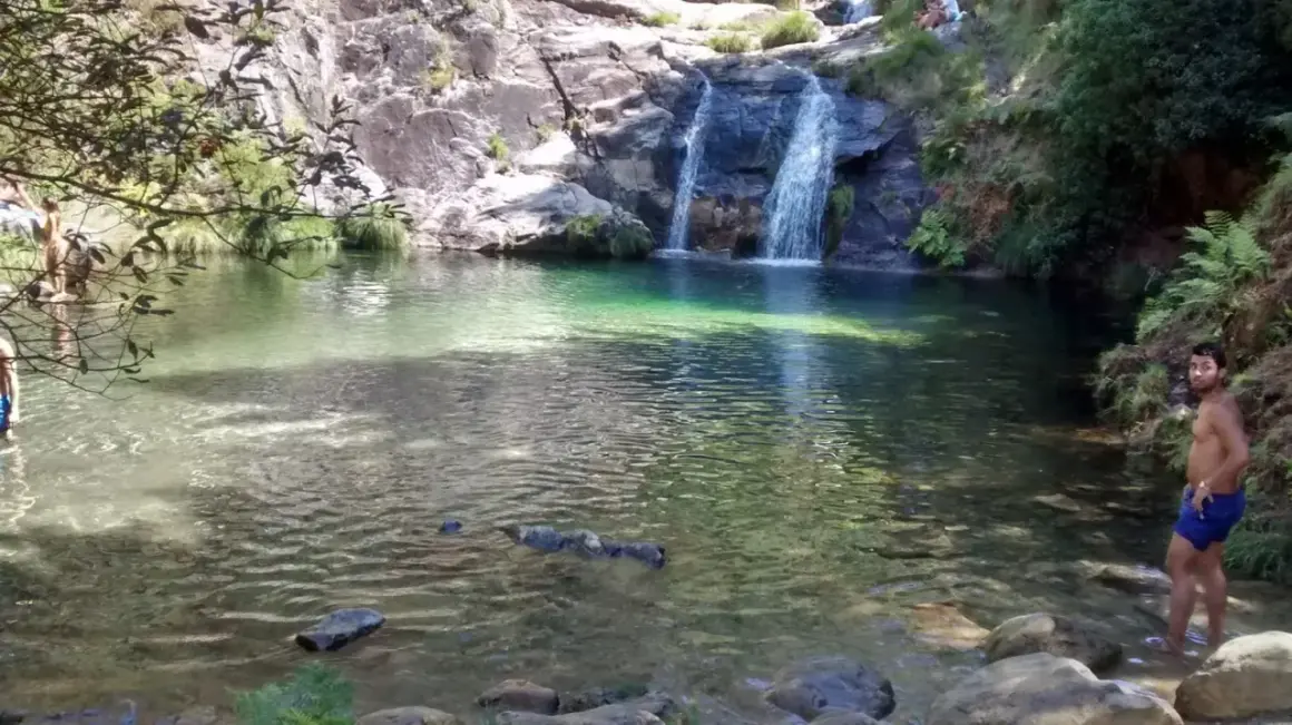Un hombre disfruta de las pozas de Mougas, con cascadas cayendo sobre rocas y agua cristalina.