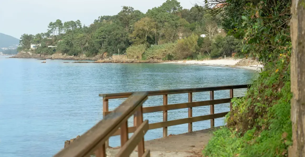 Camino de madera hacia la playa Mogor, con el mar azul y la costa verde al fondo.