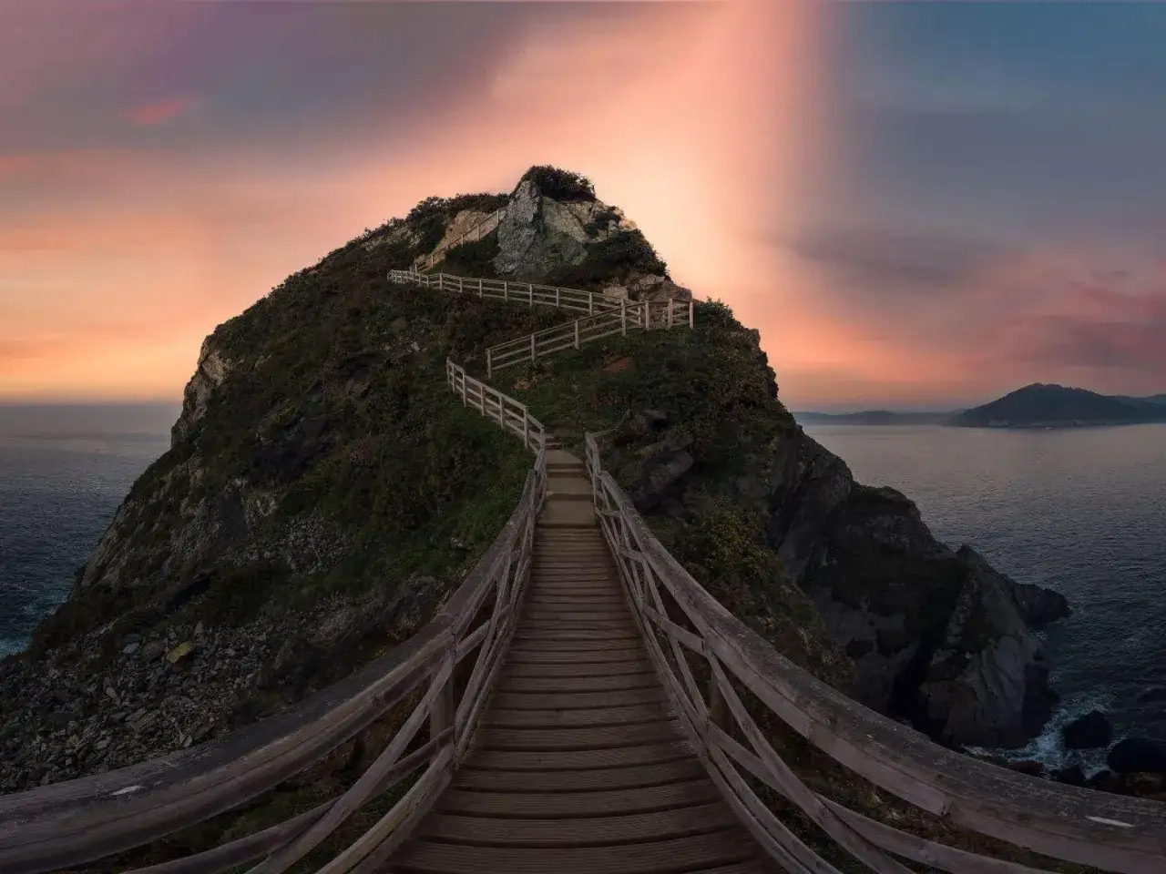 Escalera de madera serpentea hacia la cima de un acantilado rocoso con vegetación, ofreciendo vistas espectaculares de los miradores de Galicia al atardecer.