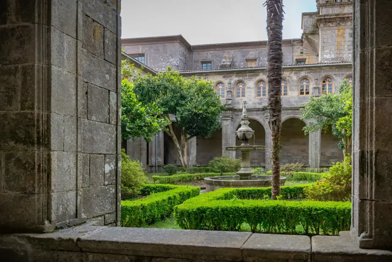 Jardín interior del monasterio de Poio, con una fuente central, setos verdes y arquitectura de piedra.
