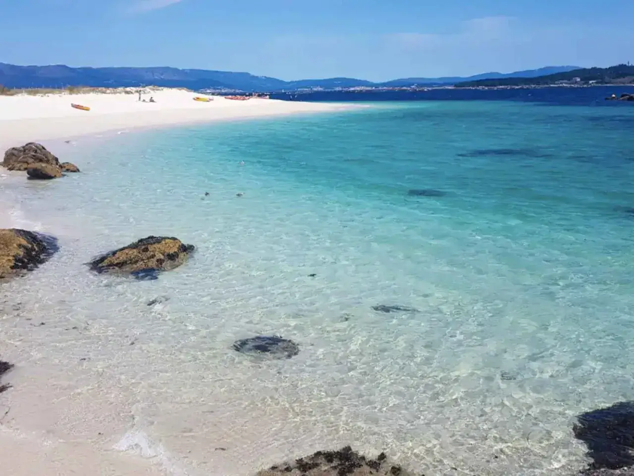Aguas cristalinas y arena blanca en la playa Paxariñas. Kayaks esperan en la orilla, invitando a explorar este paraíso.