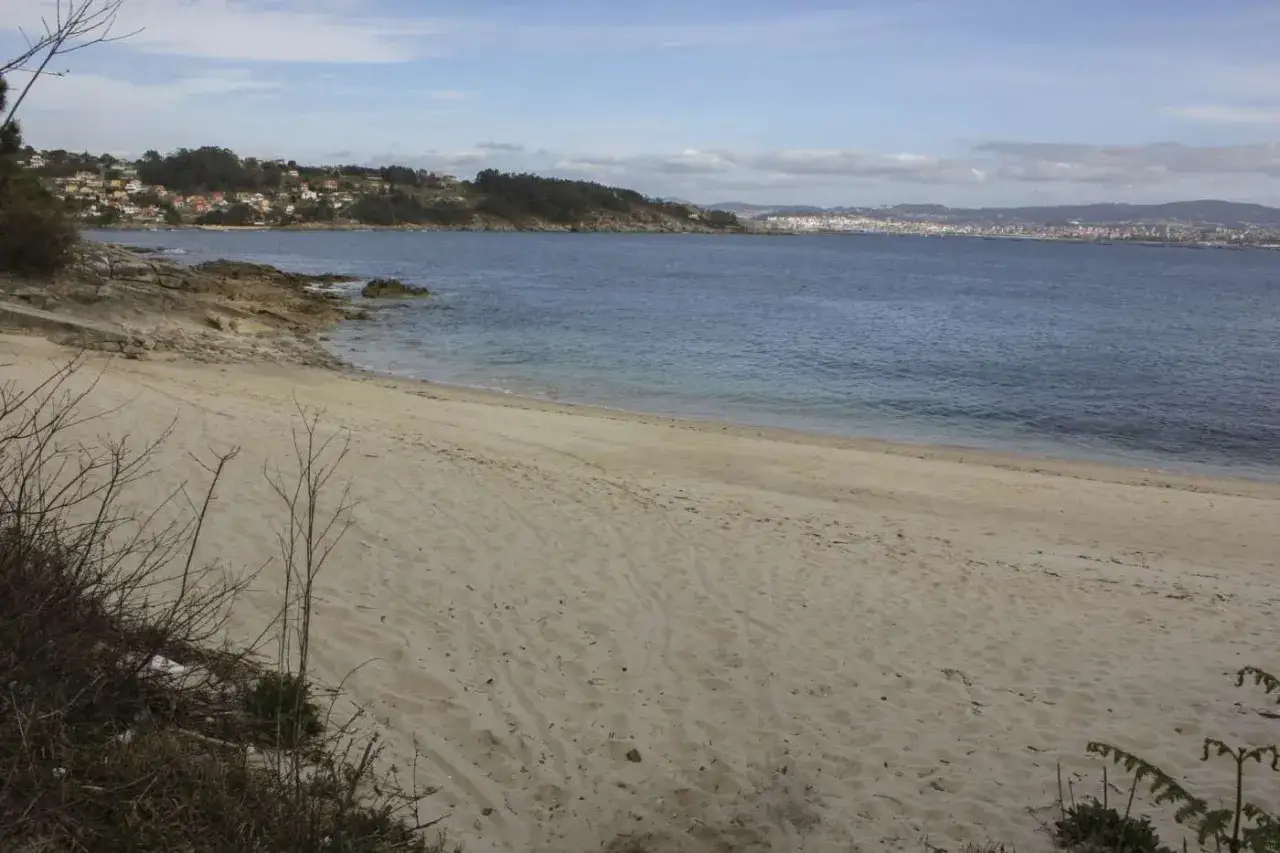 Arena dorada en la playa temperans, con el mar azul y una ciudad al fondo.