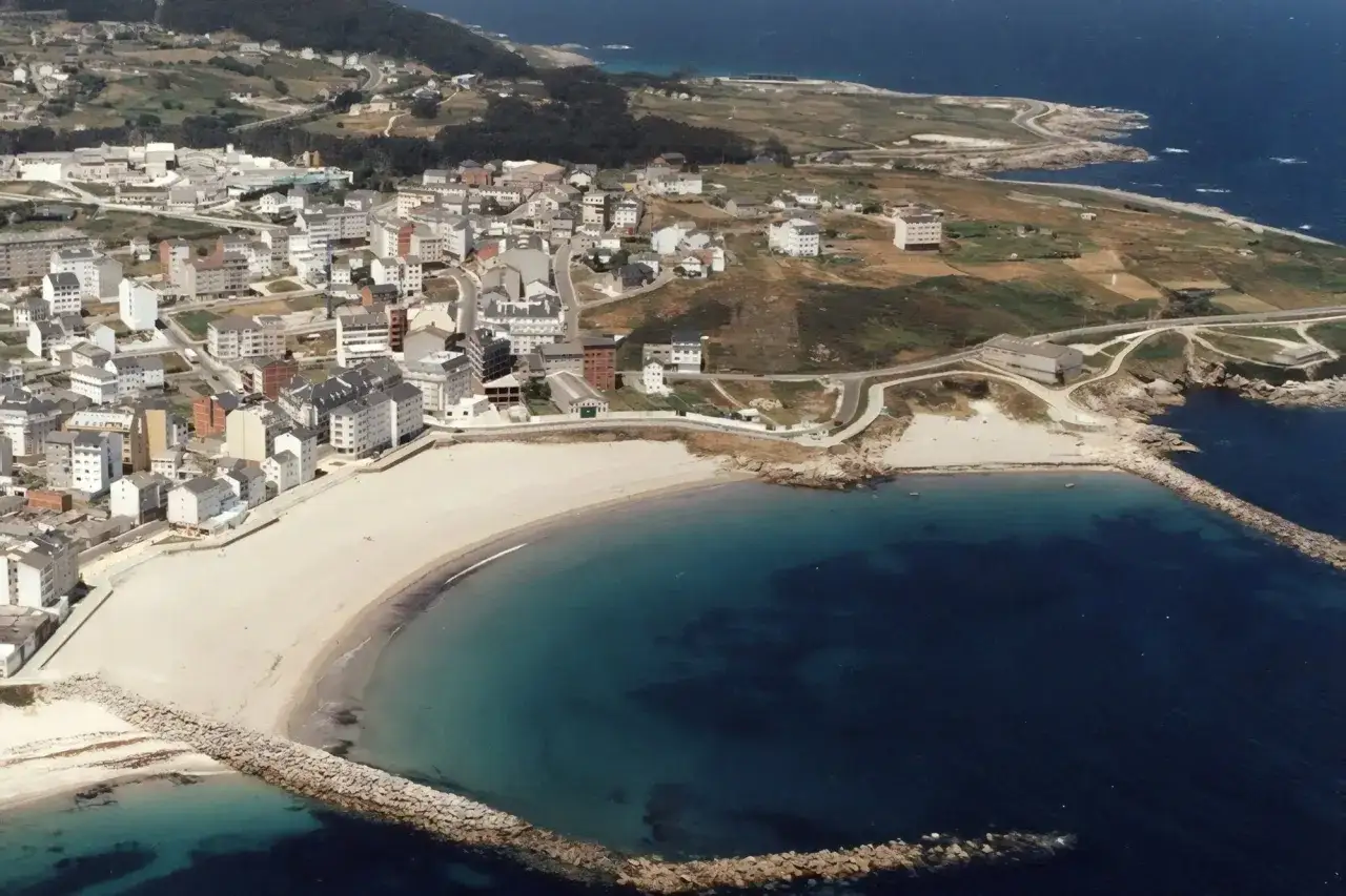 Vista aérea de la playa Penoural en Burela, con el pueblo extendiéndose hacia la costa y el mar azul intenso.