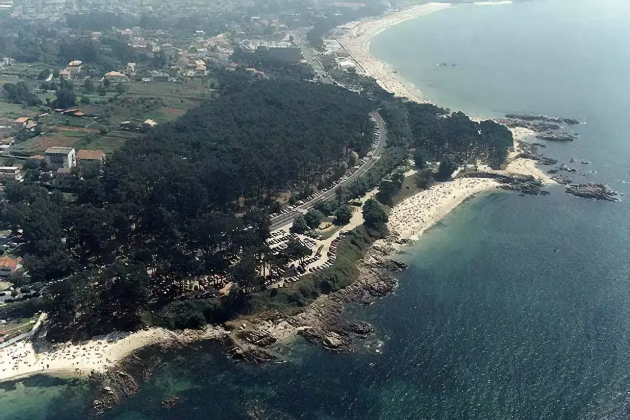 Vista aérea de la playa de los olmos en Vigo, con arena dorada, mar azul y pinos verdes. Coches aparcados en la carretera.